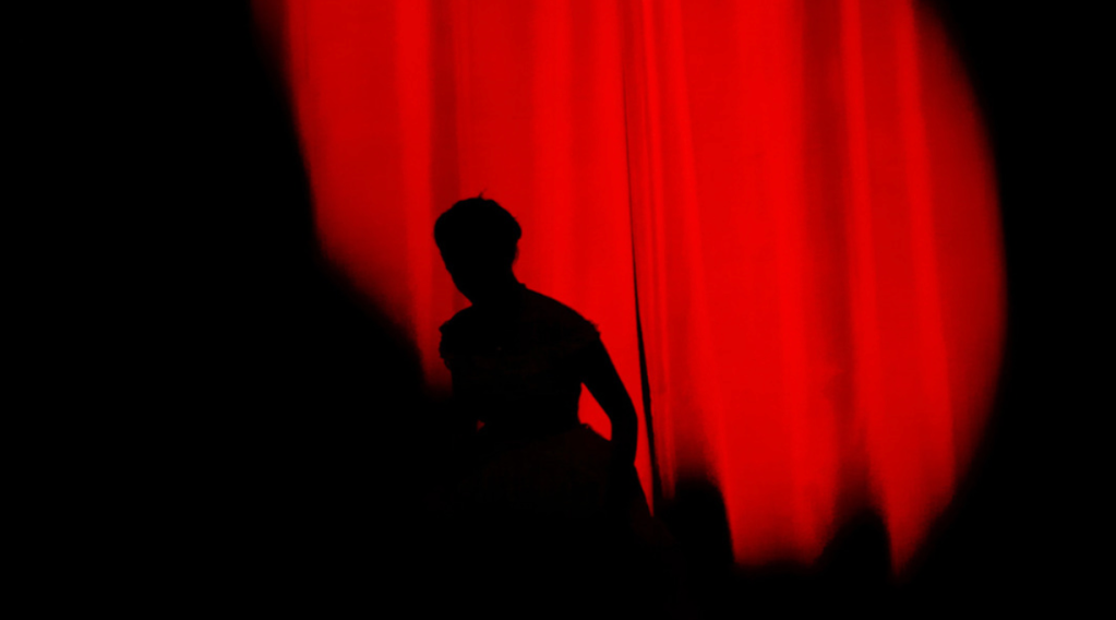 Red stage curtain with a shadow of someone running across it.